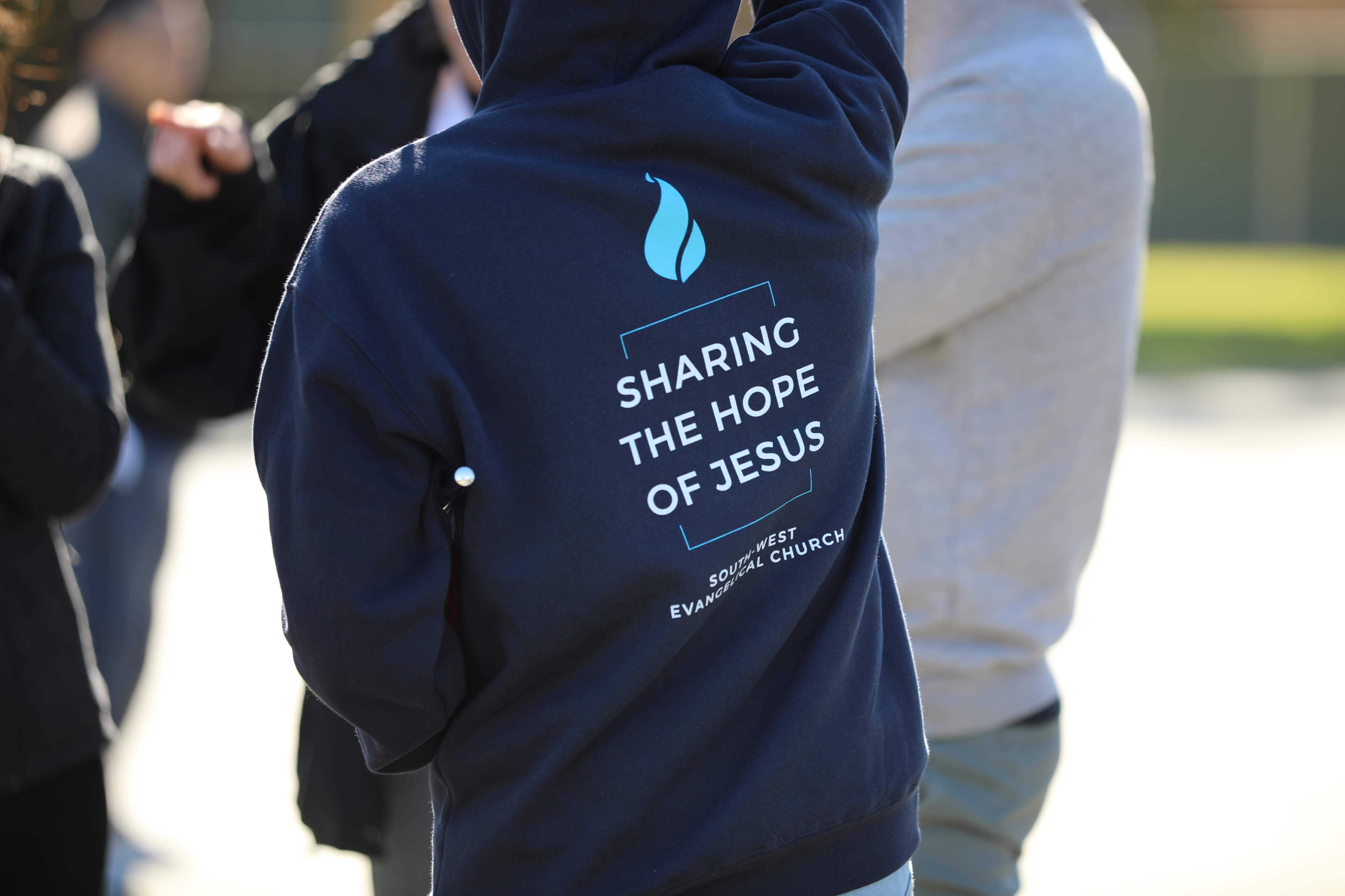 Person wearing hoodie that says, 'Sharing The Hope of Jesus'.